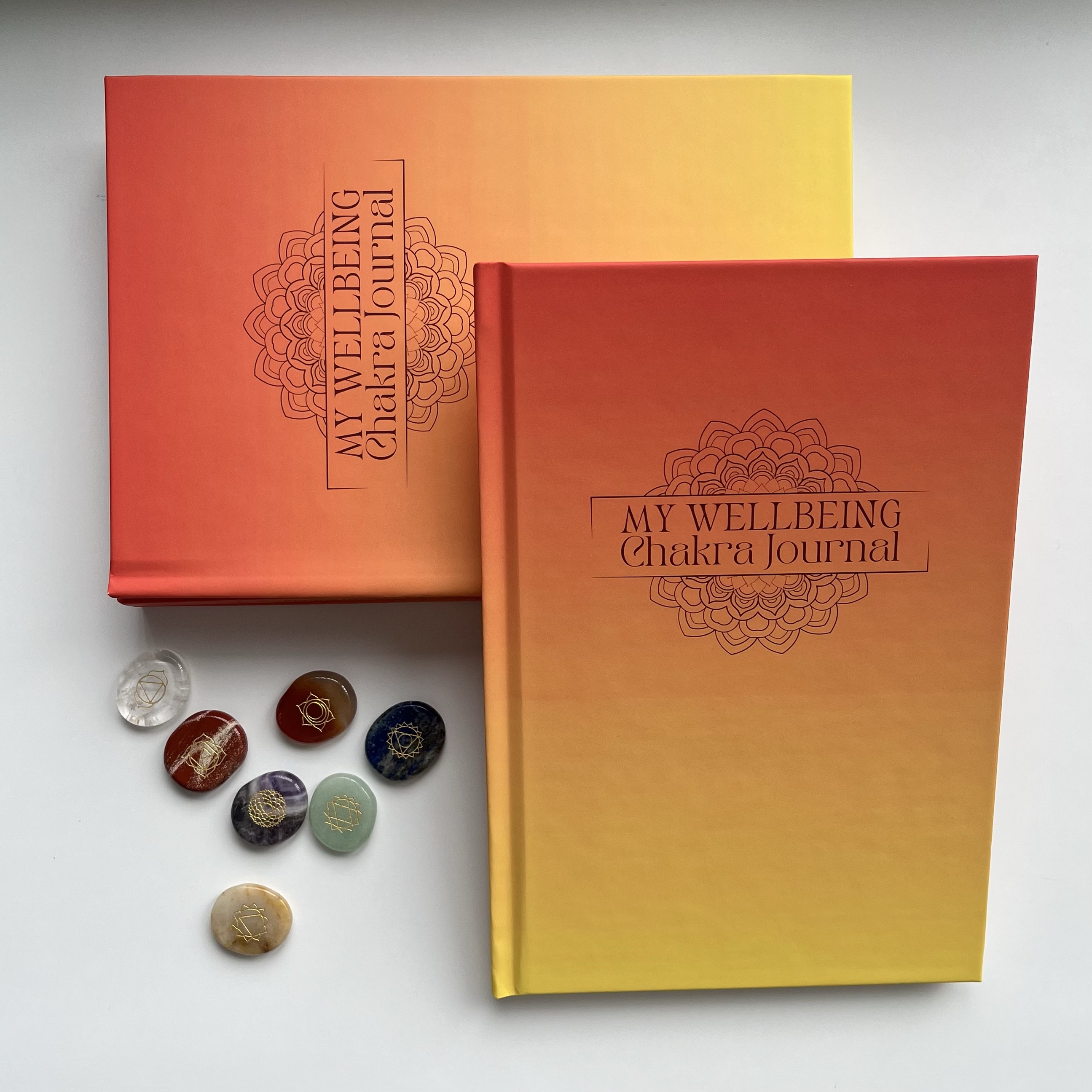 Wellbeing chakra journal leaning against other journals.  Hardback with orange and red cover with a mandala on.